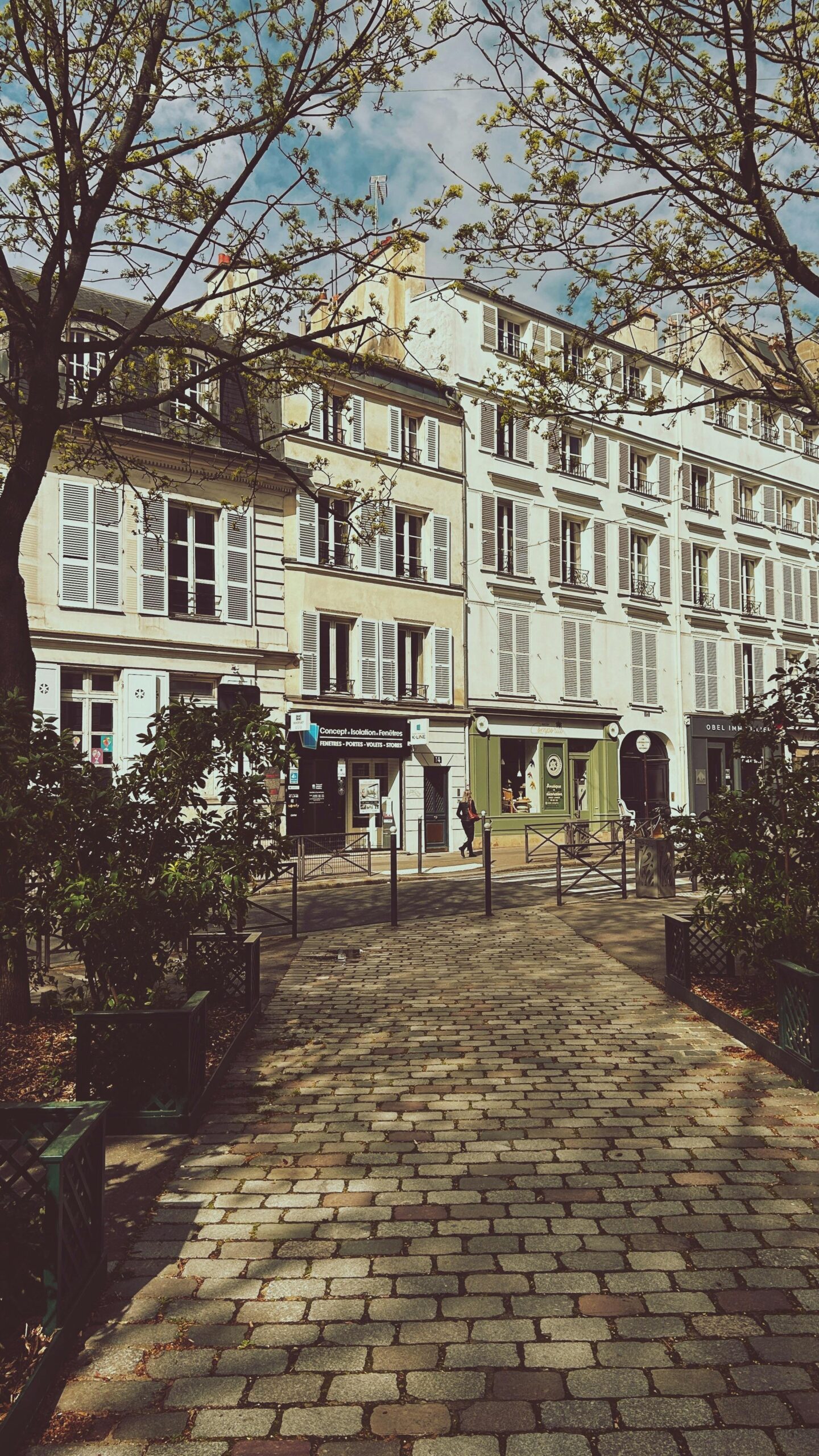 Allée pavée dans un square parisien avec verdure, bordée d’arbres et faisant face à des immeubles typiques de Paris.