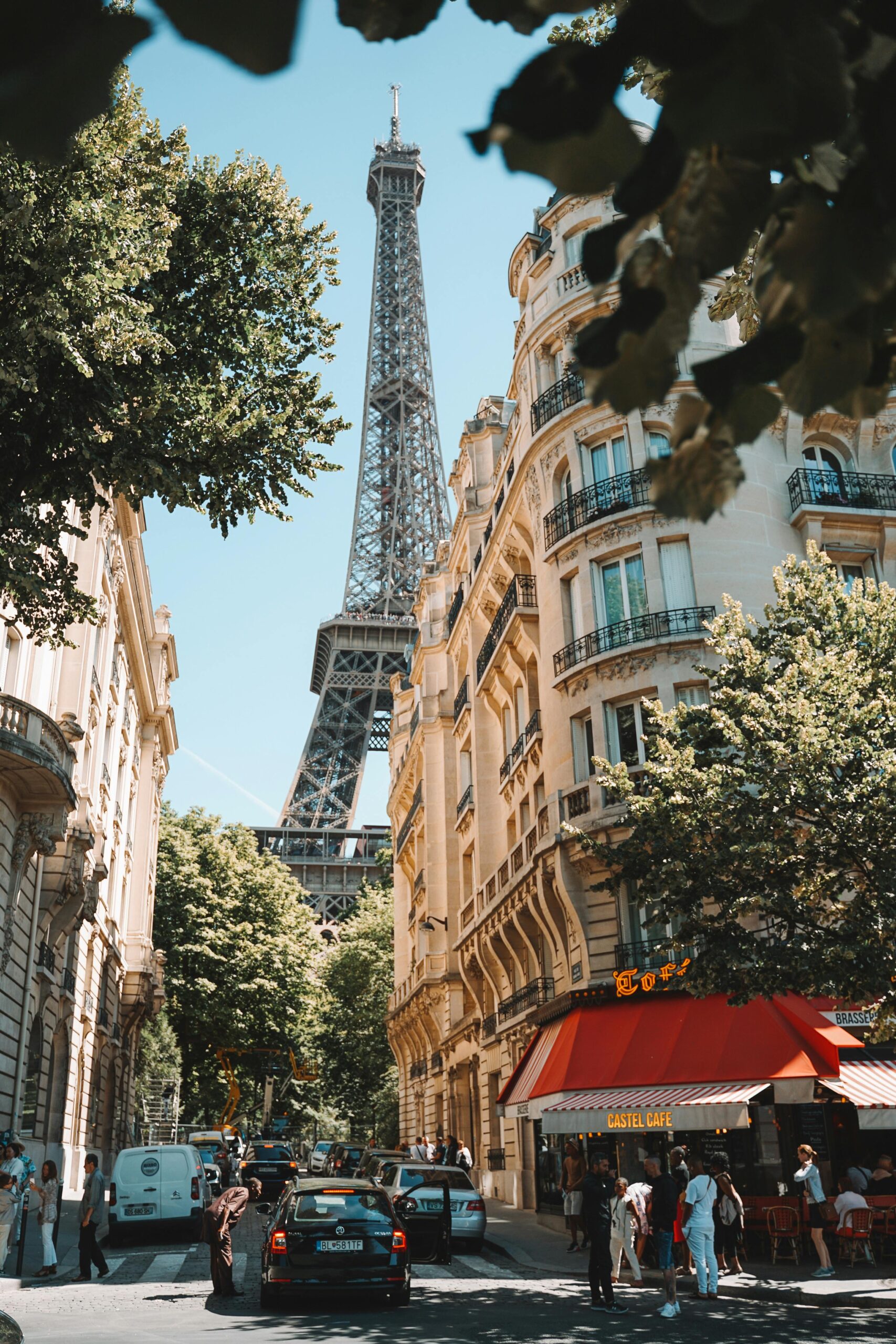 Vue sur la Tour Eiffel depuis une rue parisienne bordée d’immeubles haussmanniens et d’un café - idéal pour les acheteurs étrangers recherchant un pied-à-terre à Paris.