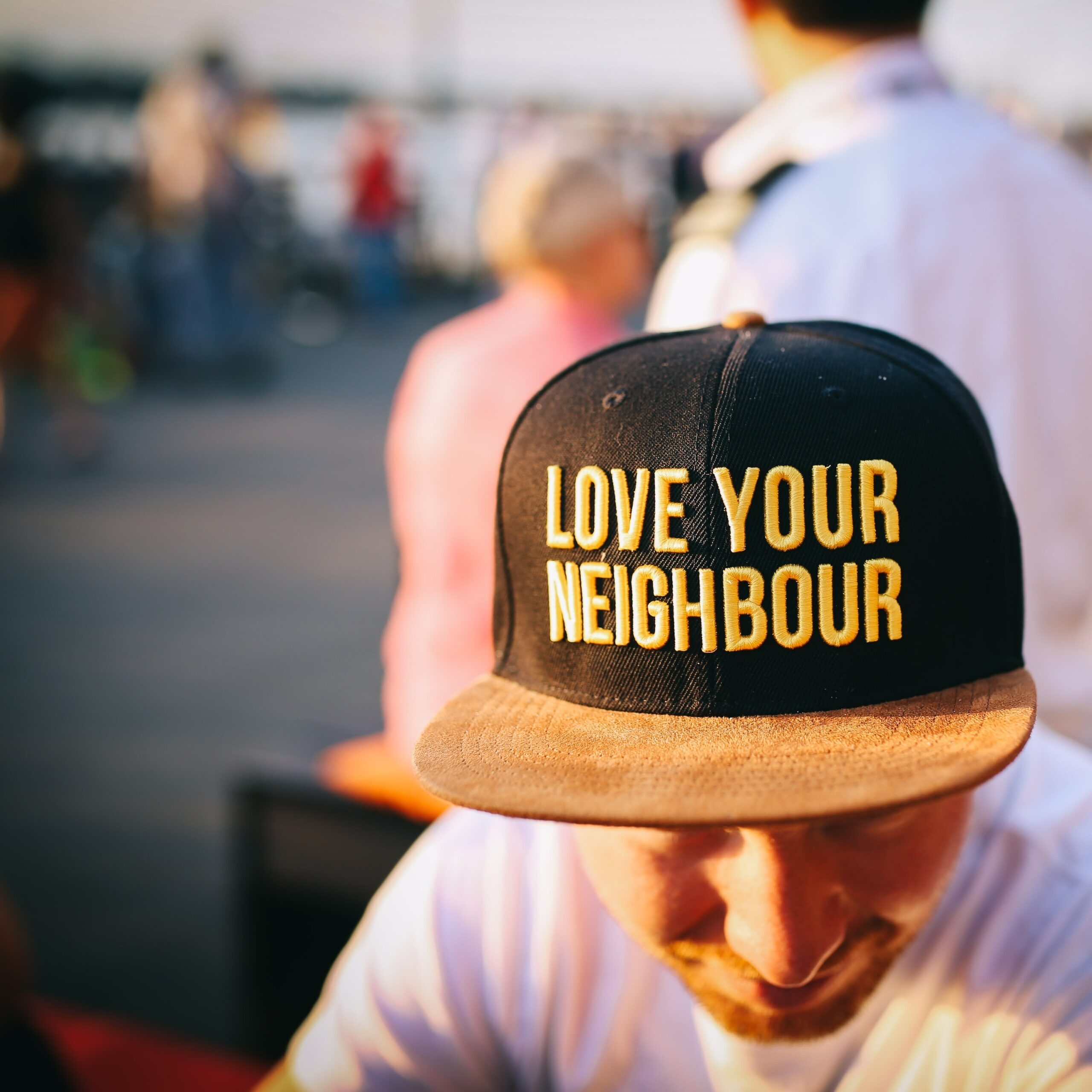 Un homme portant une casquette noire avec l’inscription ‘LOVE YOUR NEIGHBOUR’ en lettres jaunes, symbolisant la solidarité et l’esprit communautaire dans le 10e arrondissement de Paris.